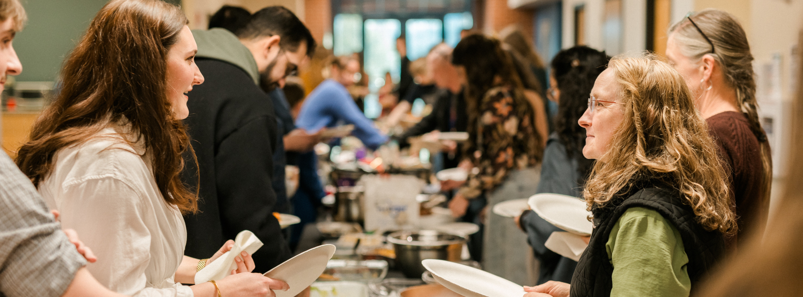 A warm, inviting church potluck scene with people gathered around tables sharing food and conversation, followed by a simple, intimate worship setting with soft lighting as individuals take turns speaking at the front of the room, creating a sense of community, reflection, and reverence.