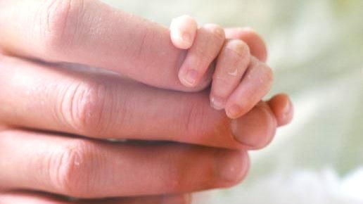 Adult hand with newborn baby fingers wrapped around the index finger